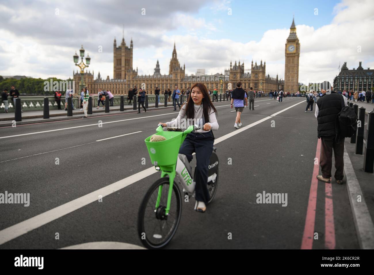 Une jeune femme asiatique passe un vélo électrique Lime au-dessus du pont de Westminster. Le pont est fermé aux voitures pendant la cérémonie de la Reine couché dans l'État. Banque D'Images