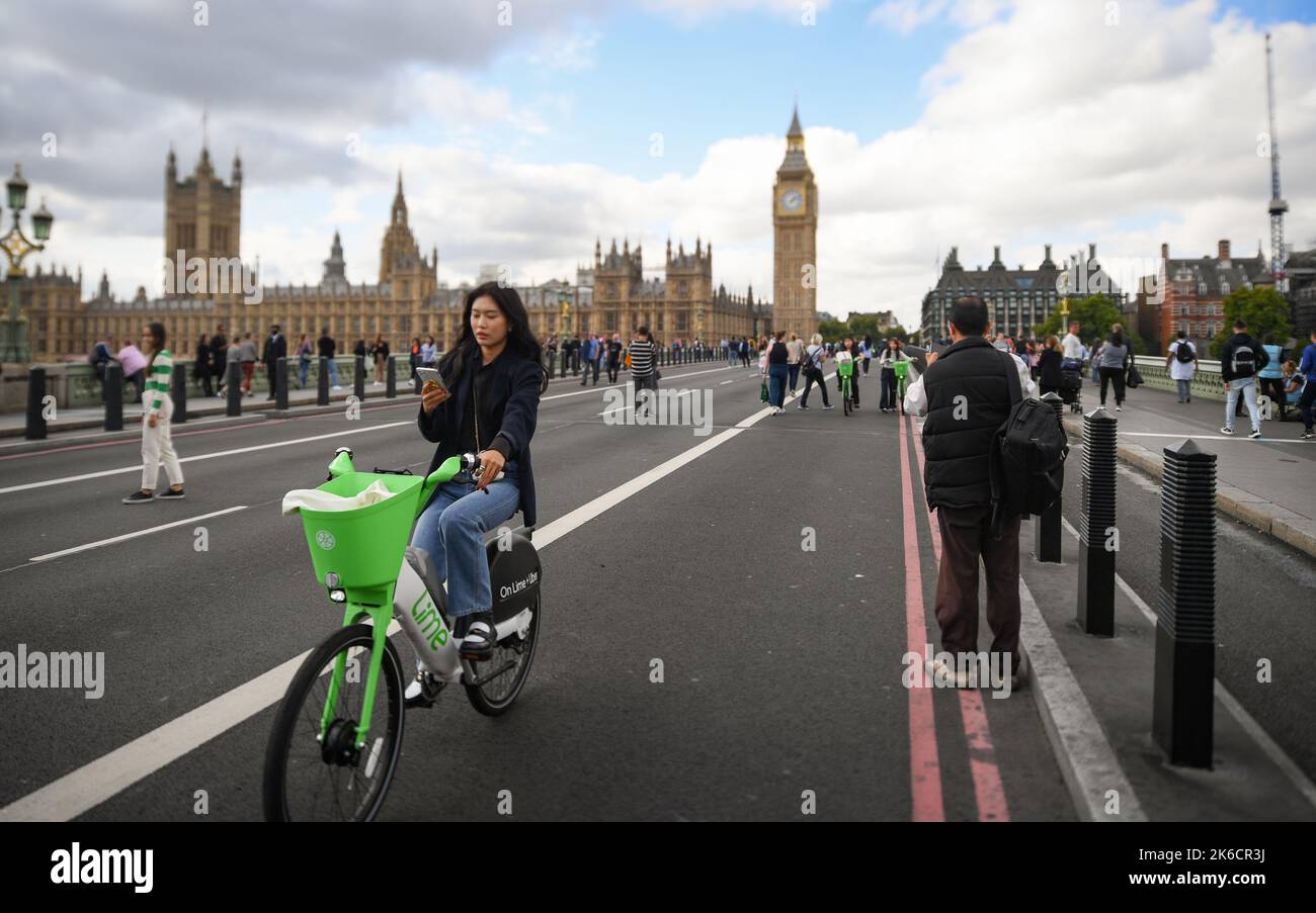 Une jeune femme regarde un téléphone mobile tout en faisant un vélo électrique Lime au-dessus de Westminster Bridge Londres Royaume-Uni. Banque D'Images
