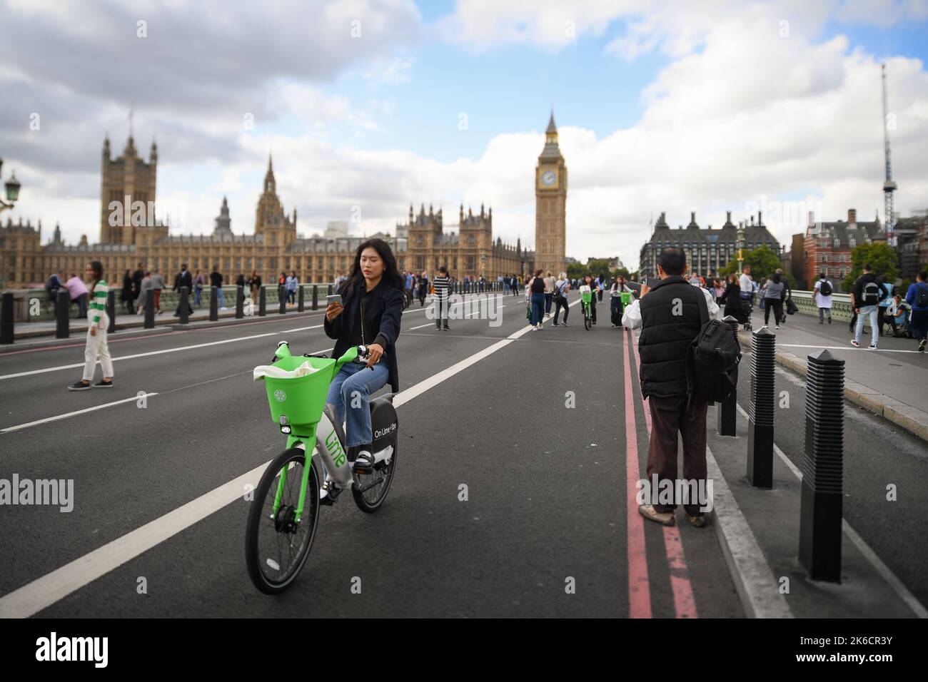 Une jeune femme regarde un téléphone mobile tout en faisant un vélo électrique Lime au-dessus de Westminster Bridge Londres Royaume-Uni. Banque D'Images
