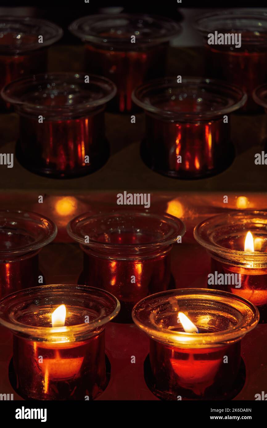 Bougies de cire votive blanche allumée et éteinte utilisées pour une prière chrétienne sur un contenant en métal avec des flammes calmes sur un fond sombre à un stand i Banque D'Images