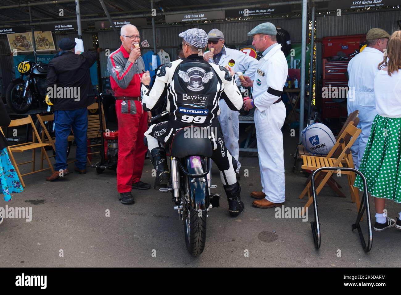 Rider Duncan Fitchett ou Jeremy McWilliams assis sur un Norton Daytona Manx 1952 avec trois mécaniciens mangeant des crèmes glacées, Goodwood Revival, Chichester, Banque D'Images