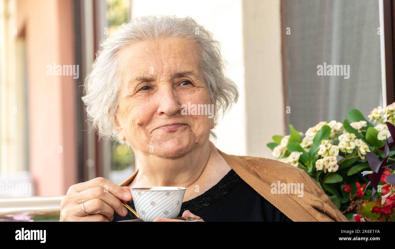 Une vieille femme souriante boit du café turc et se détend sur le balcon. Femme âgée en 70s souriant et appréciant le temps. Banque D'Images