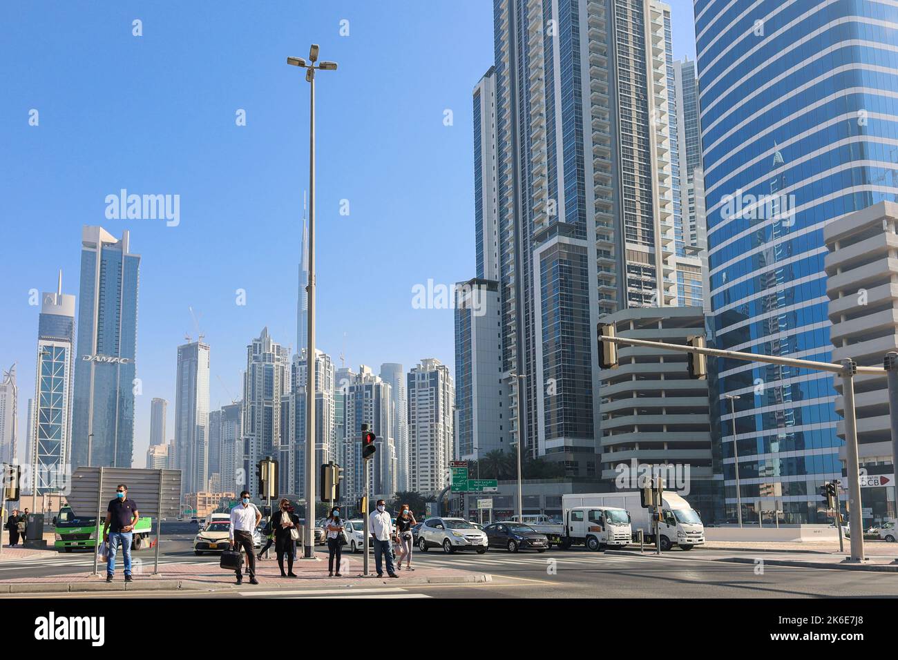 Eau, Dubaï - 27 novembre 2021 : les gens marchent le long de la traversée piétonne dans le centre d'affaires de Dubaï. Les hommes en costume et les masques médicaux se précipitent pour travailler sur fond d'énormes gratte-ciel. Photo de haute qualité Banque D'Images