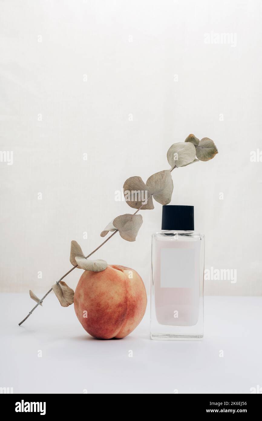 Bouteille cosmétique, branche de fruits de pêche et d'eucalyptus sur table blanche. Beauté, mode concept. Vue avant. Banque D'Images