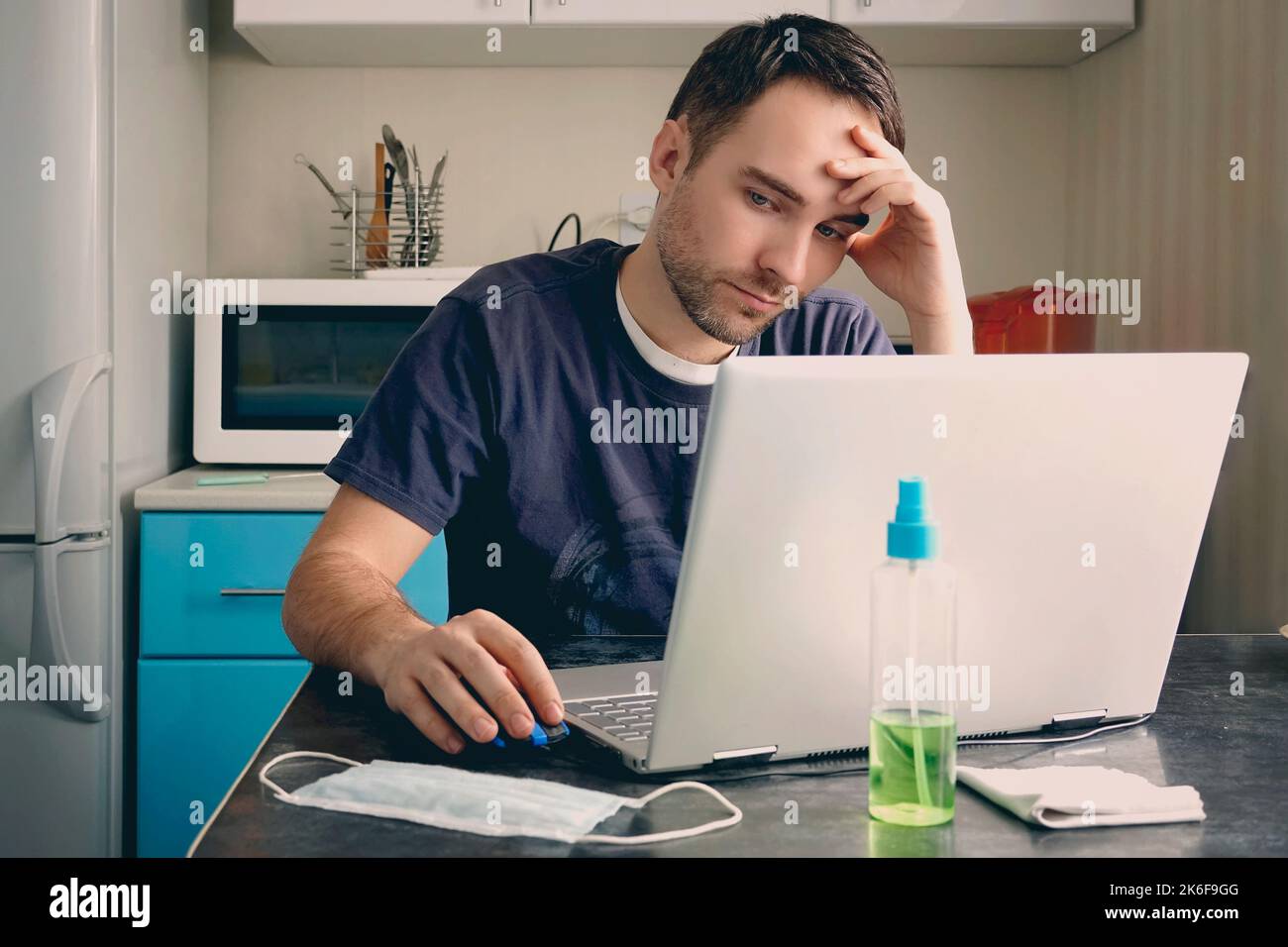 Un homme de designer malsain porte un masque assis au bureau près d'un ordinateur portable. Le jeune homme d'affaires se sent mal à travailler pendant le coronavirus ou COVID19 pandémie infectiou Banque D'Images