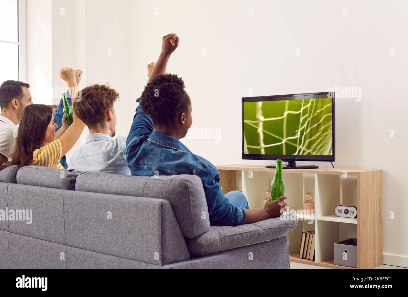 Des amis heureux et variés assis sur un canapé, regardant le football à la télévision et buvant de la bière Banque D'Images