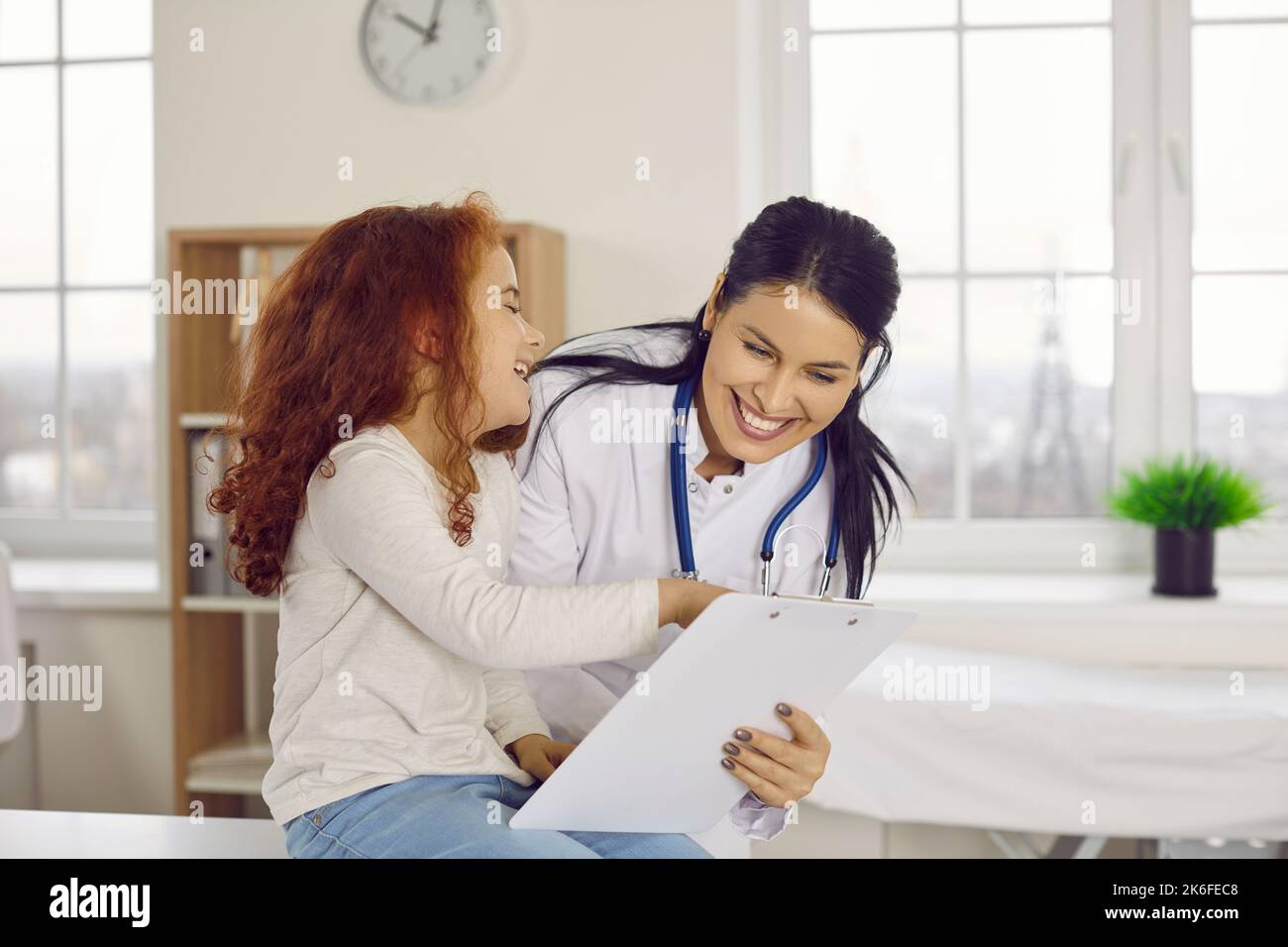 Sympathique femme souriante pédiatre s'amusant avec une petite fille dans son bureau d'hôpital. Banque D'Images