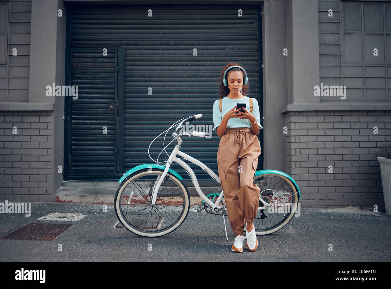 Casque, femme et téléphone avec vélo dans la ville écouter de la musique ou balado en plein air en été avec un look tendance. Écologique Banque D'Images