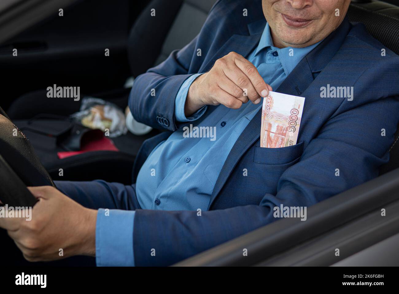 Le conducteur, un homme en costume cher, sort 5 000 roubles de sa poche. Le concept de corruption sur les routes. Un député donne un pot-de-vin à un corru Banque D'Images