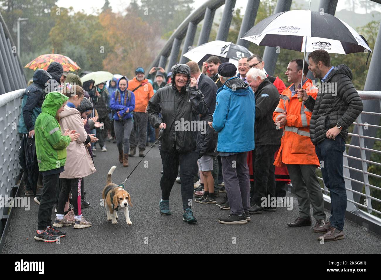 New Road, Kendal - 14 octobre 2022 - Minnie Ker, 61 ans d'Ayrshire, en Écosse, a été la première personne à marcher un chien (appelé Bassett) à travers le pont Gooseholme à Kendal, Minnie a déclaré: "C'était un honneur et un plaisir". Le pont a officiellement ouvert ses portes le vendredi 14 octobre par le président du conseil du comté de Cumbria (CCC), Cllr Andy Connell, avec des enfants de l'école de Stramongate à proximité (tous autorisés pour les photos). Le député Tim Farron a aussi fait une apparition. La passerelle, qui coûte 2 millions de livres, a remplacé un vieux pont plus petit qui a été endommagé à Storm Desmond qui a frappé la ville en 2015, causant des inondations dévastatrices. Le Banque D'Images