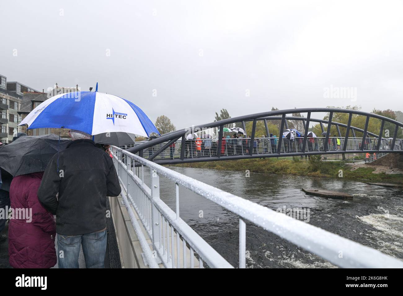 New Road, Kendal - 14 octobre 2022 - Une file d'attente sous la pluie pour traverser le pont Gooseholme à Kendal qui a officiellement ouvert le vendredi 14 octobre par le président du conseil du comté de Cumbria (CCC), Cllr Andy Connell avec des enfants de l'école Stramongate à proximité (tous autorisés pour les photos). Le député Tim Farron a aussi fait une apparition. La passerelle, qui coûte 2 millions de livres, a remplacé un vieux pont plus petit qui a été endommagé à Storm Desmond qui a frappé la ville en 2015, causant des inondations dévastatrices. La structure monstrueuse a été mise en place en juillet avec des touches finales réalisées au cours des derniers mois. CCC, W Banque D'Images