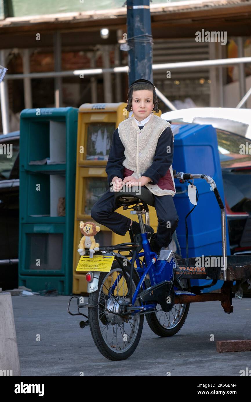 Un garçon juif orthodoxe est assis à l'arrière sur le siège d'un vélo de livraison. Sur Lee Avenue à Brooklyn, New York. Banque D'Images