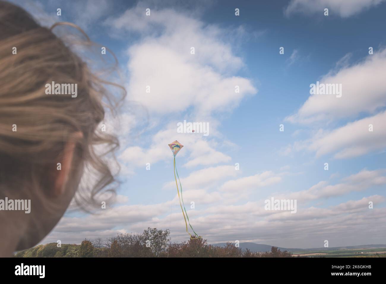 gros plan de filles tête vue arrière gérant un cerf-volant dans le ciel Banque D'Images