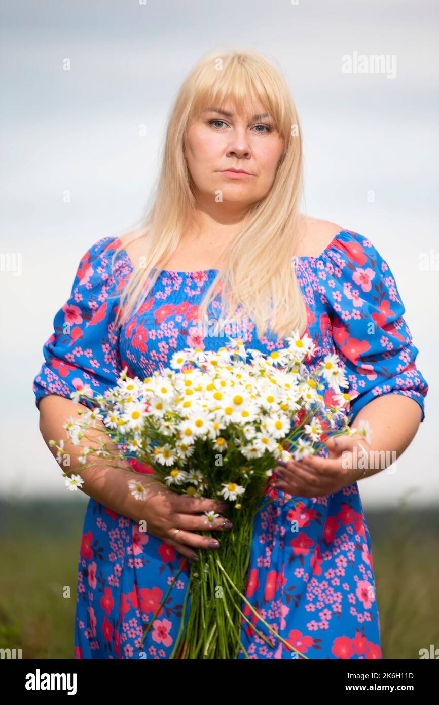 Belle femme de taille plus avec des cheveux blancs dans une robe d'été posant à l'extérieur avec des pâquerettes. Fille de chubby dans un pré avec des fleurs. Banque D'Images