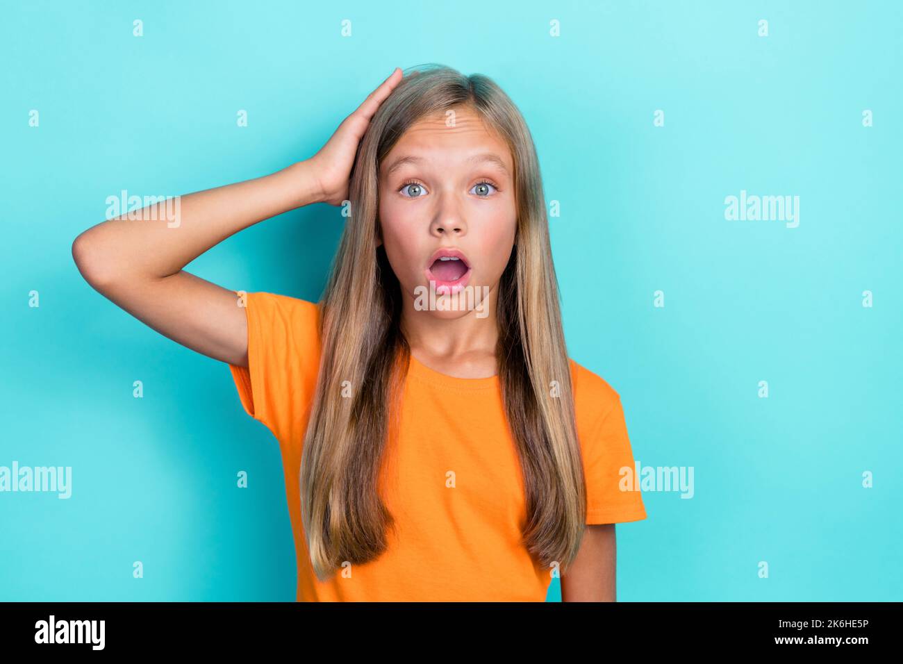 Gros plan photo de jeune fille adorable drôle écolière enfant porter t-shirt orange bouche ouverte tête de contact inattendue peur isolée sur fond bleu-vert Banque D'Images