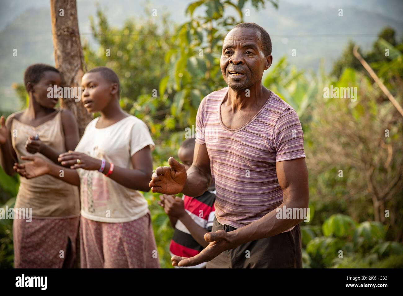 Un homme africain heureux chante avec sa famille devant sa maison dans les montagnes Rwenzori en Ouganda, dans le district de Kasese, en Afrique de l'est. Banque D'Images