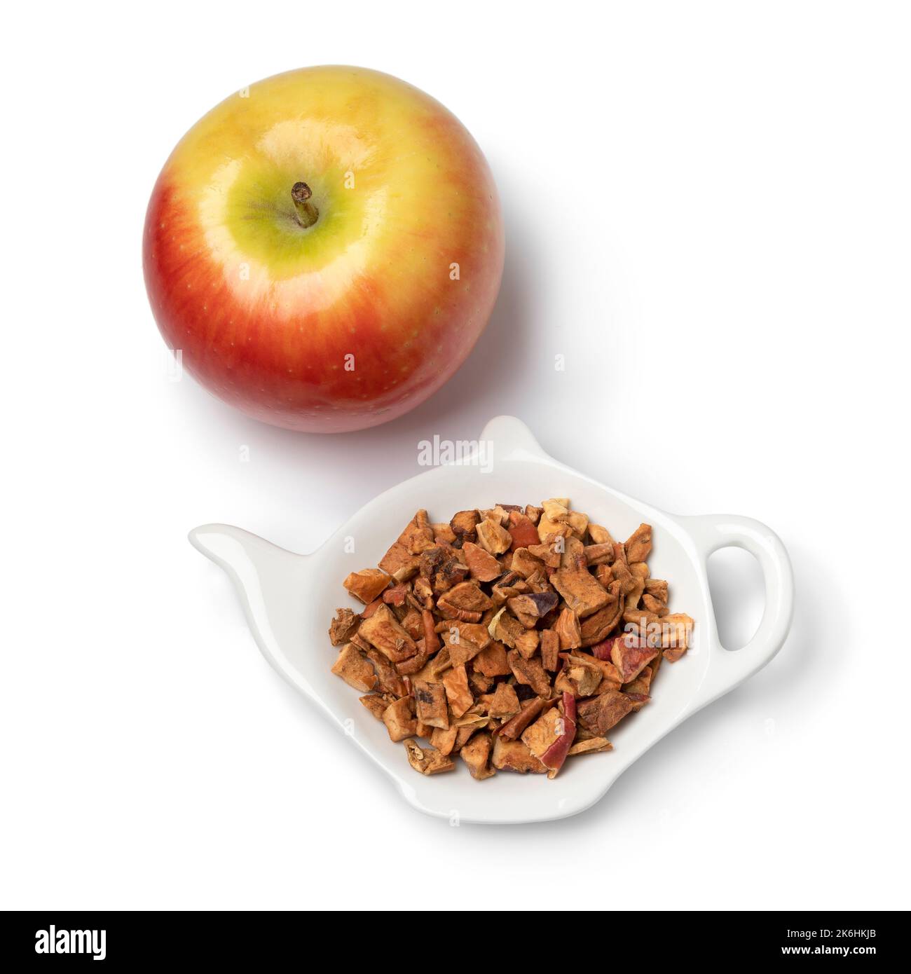 Des morceaux de pomme séchés sur un bol en forme de théière se ferment et une pomme fraîche dans le fond isolé sur fond blanc Banque D'Images