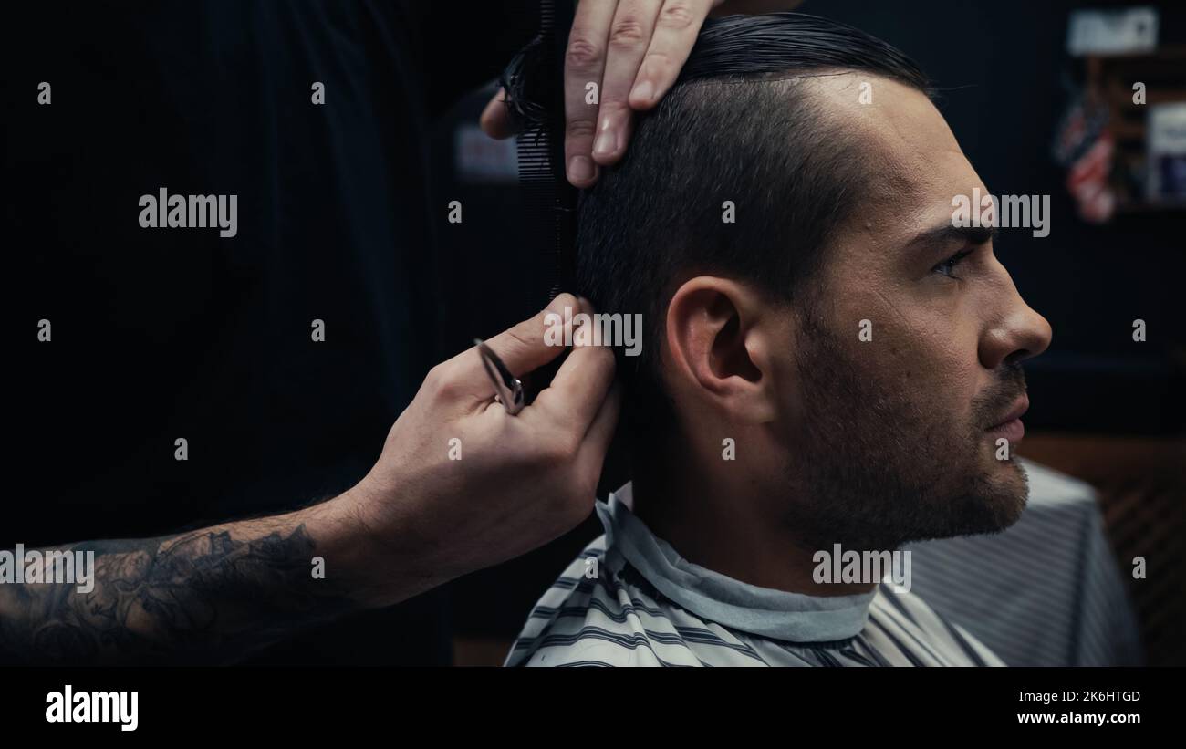 Coiffeur tenant des ciseaux et peignant les cheveux de l'homme dans le cap de coiffure dans le salon, image de stock Banque D'Images
