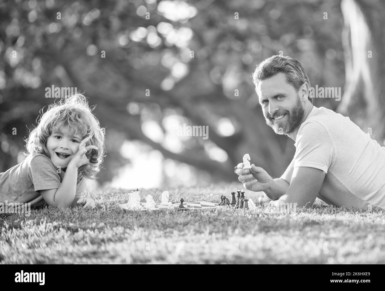 bonne famille de père et fils enfant jouant aux échecs sur l'herbe verte dans le parc extérieur, chessman. Banque D'Images
