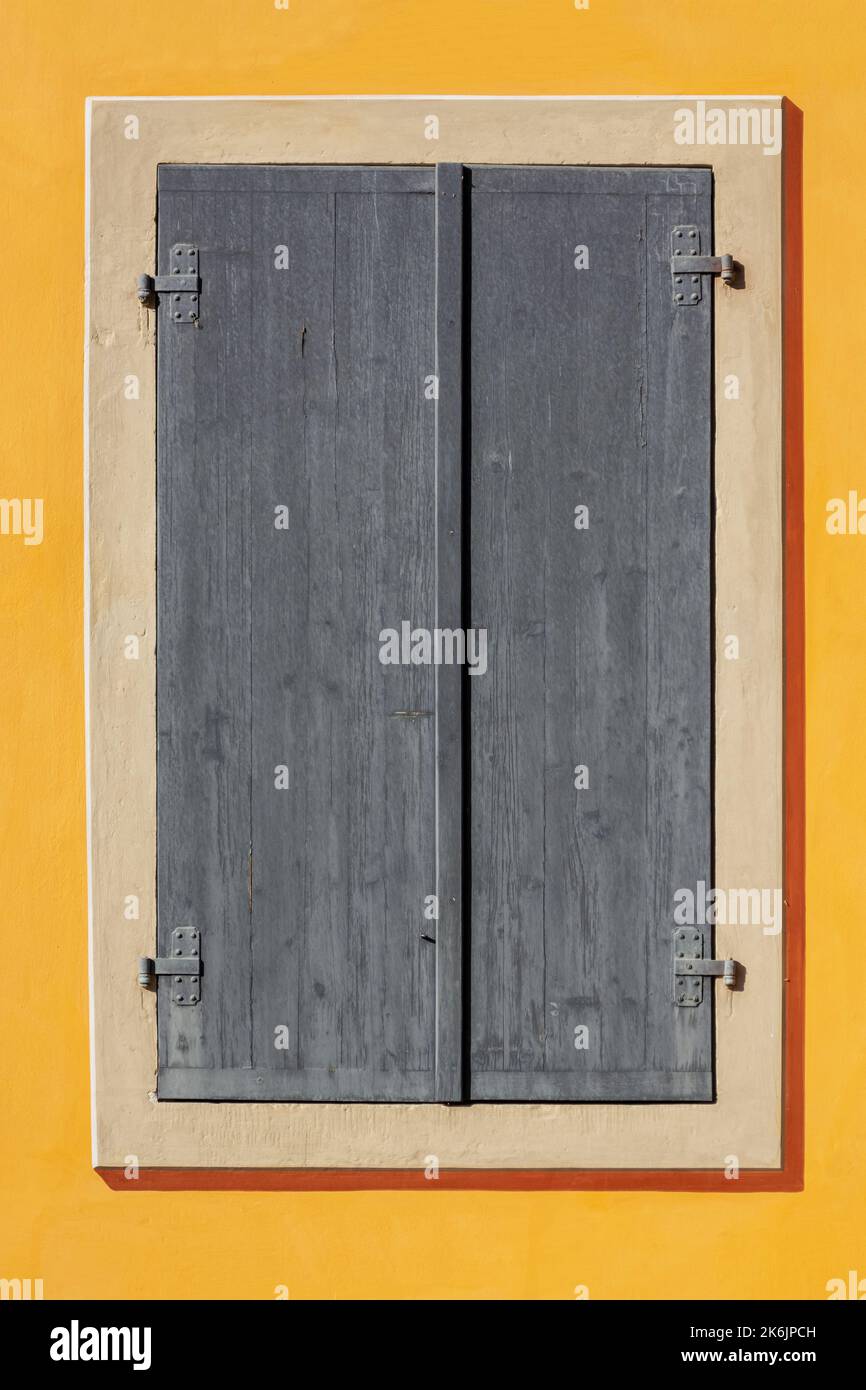 La fenêtre rectangulaire est recouverte de volets en bois gris contre un mur jaune. De la série fenêtre du monde. Banque D'Images