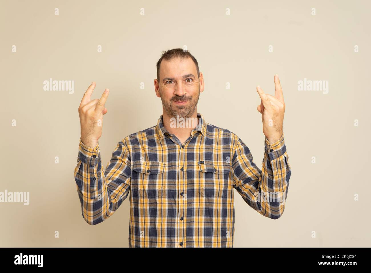 Le portrait d'un homme sur fond beige montre un geste avec ses mains Rock n Roll. Le concept de langage corporel. Banque D'Images