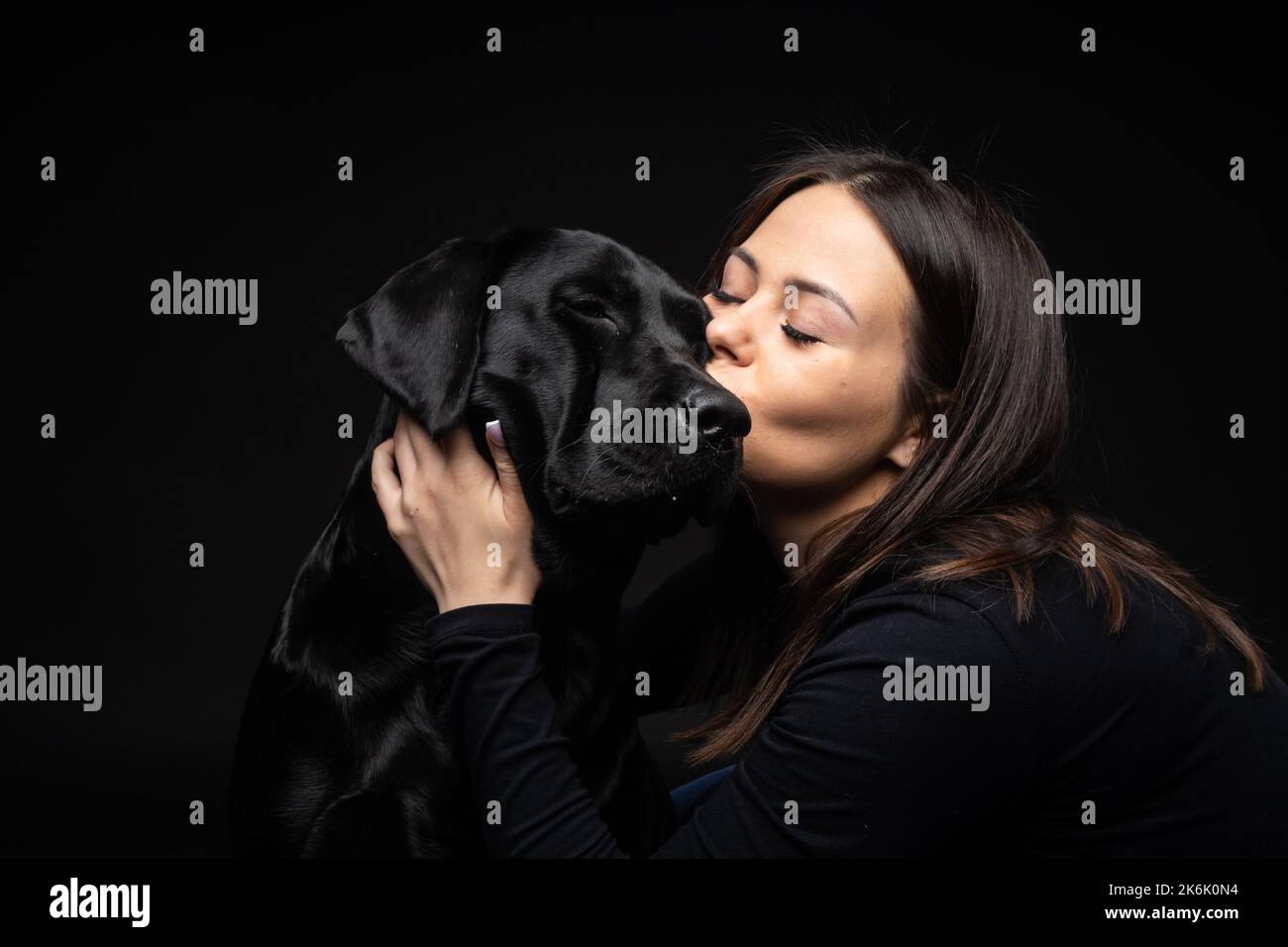 Une fille tient un chien Labrador Retriever dans ses bras. Prise en gros plan dans un studio photo, sur un dos noir Banque D'Images