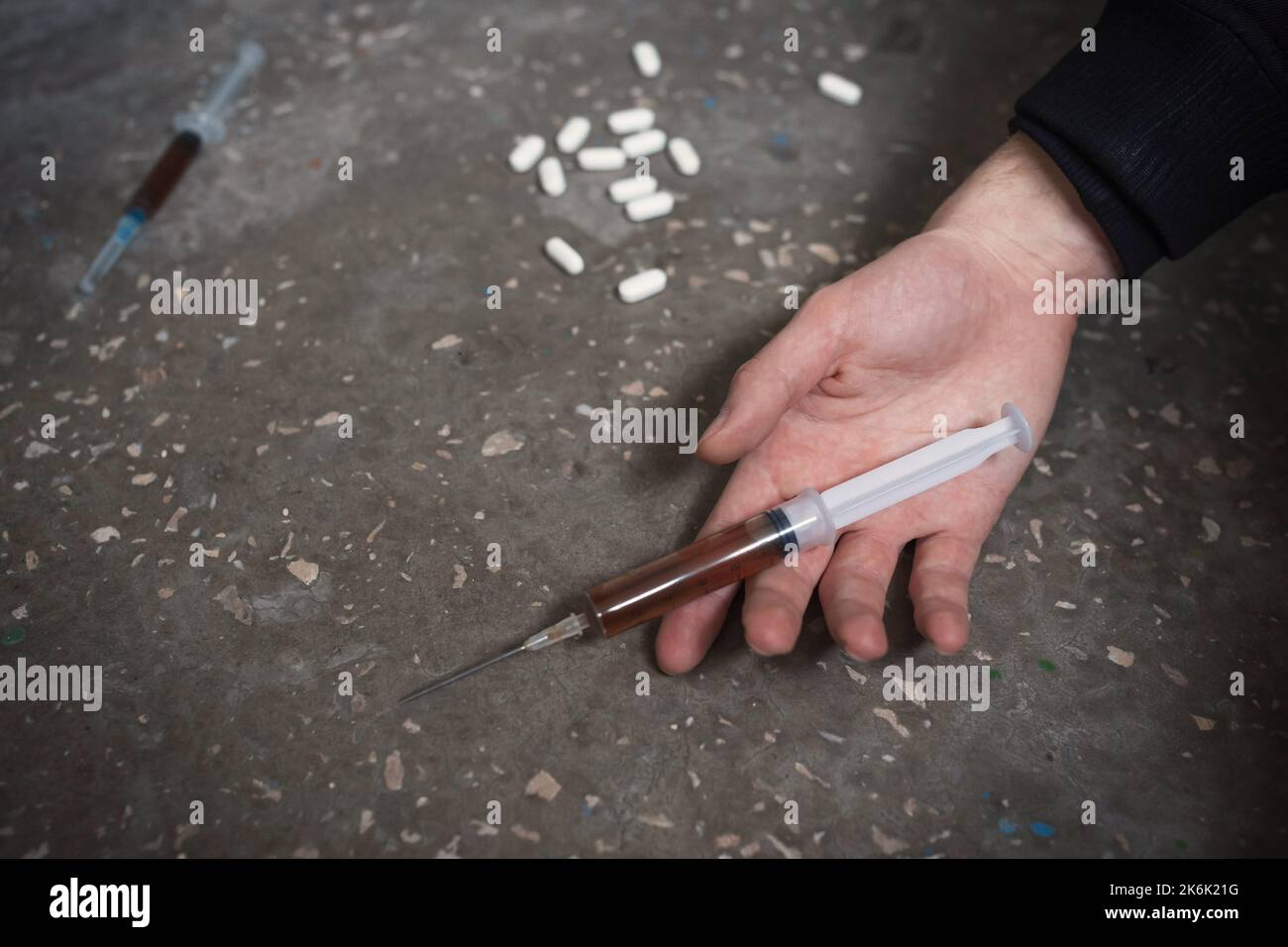 Main du narcotiste avec la seringue sur le sol. Le concept de l'abus de drogues, surdose. Banque D'Images