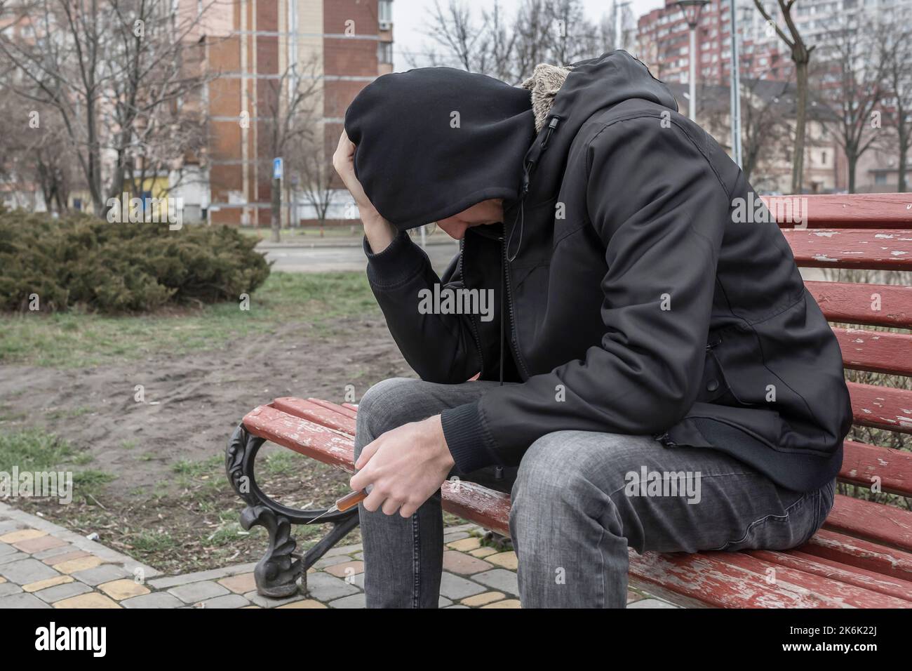 Addict connaissant une crise de toxicomanie, à l'extérieur avec une seringue dans sa main. Style de vie, addiction concept. Banque D'Images
