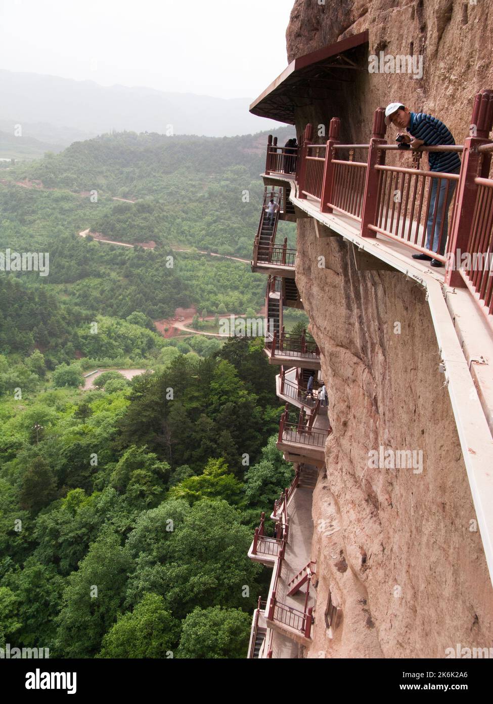 Les escaliers et la gravité défiant la grande passerelle / escaliers et les allées attachées à la roche fine ont permis aux visiteurs de contact étroit avec les figures d'argile et les anciennes sculptures en pierre. Le site de représentations / figures bouddhistes représentations et d'images de Bouddha (certaines semblent être très récemment restaurées en béton) sur la face rocheuse des Grottes de Maijishan, autrefois romanisé comme Maichishan, une série de 194 grottes coupées sur le côté des montagnes de Majishan à Tianshui, province de Gansu, Chine. PRC. (67/125) Banque D'Images