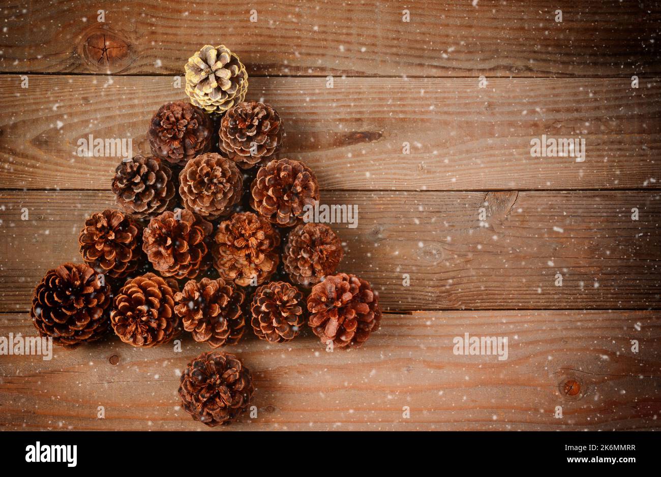 Cônes de pin disposés en forme de sapin de Noël sur un fond de parquet rustique avec effet neige et vignette. Banque D'Images