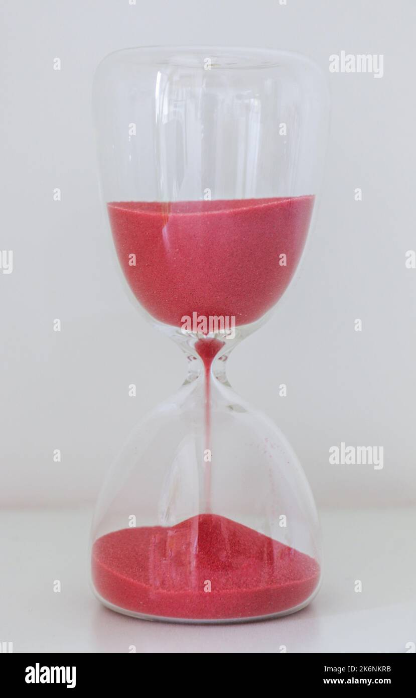 Un sablier sur fond blanc, avec du sable rouge qui glisse, mesurant le passage du temps, compte à rebours jusqu'à une date limite Banque D'Images