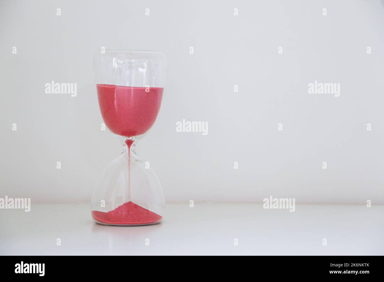 Un sablier isolé à gauche de fond blanc, sable rouge glissant loin, mesurant le passage du temps, courant à court de concept de temps Banque D'Images