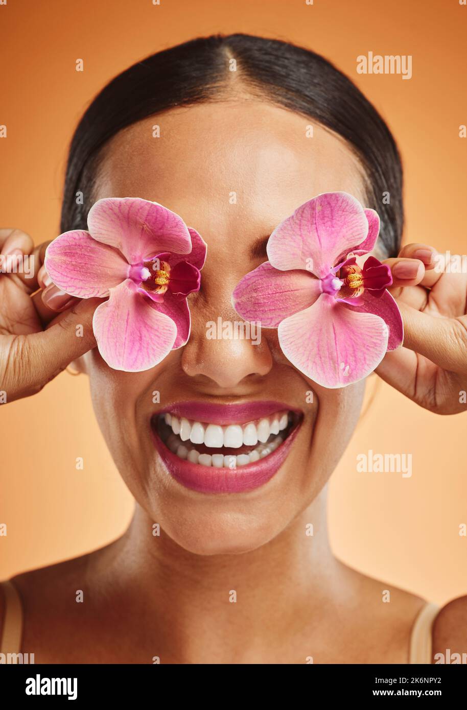 Fleur d'orchidée, femme d'art créatif et de beauté avec maquillage, cosmétique et sourire sur le visage sur fond orange. Happy, florale et comique femme Banque D'Images