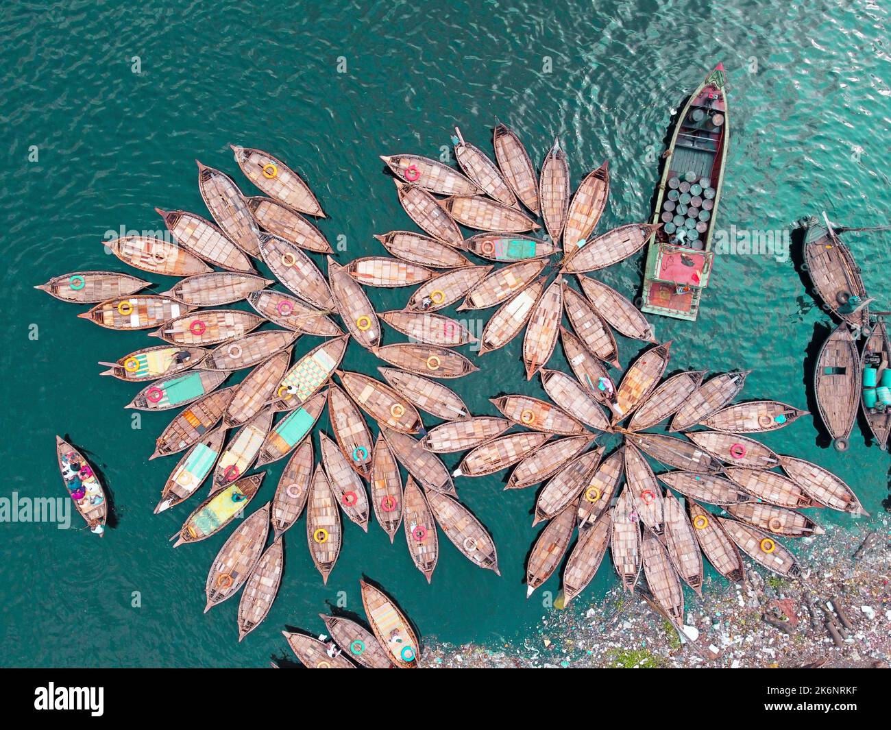 Des centaines de bateaux en bois détournent leurs amarres dans des motifs qui ressemblent aux pétales de fleur pour un trajet matinal très chargé sur le fleuve Buriganga. Banque D'Images