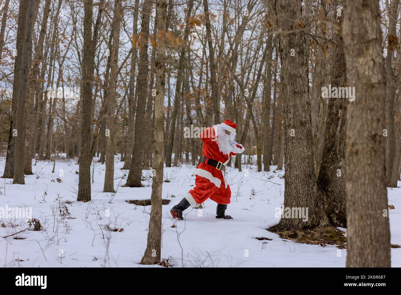 Avec des cadeaux de Noël en sac rouge dans ses mains, le Père Noël marche à travers la forêt autour de vues sur la neige blanche Banque D'Images