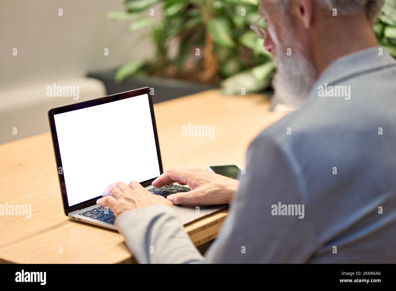 Ancien homme d'affaires enseignant dactylographiant sur ordinateur portable avec écran blanc maquette. Banque D'Images