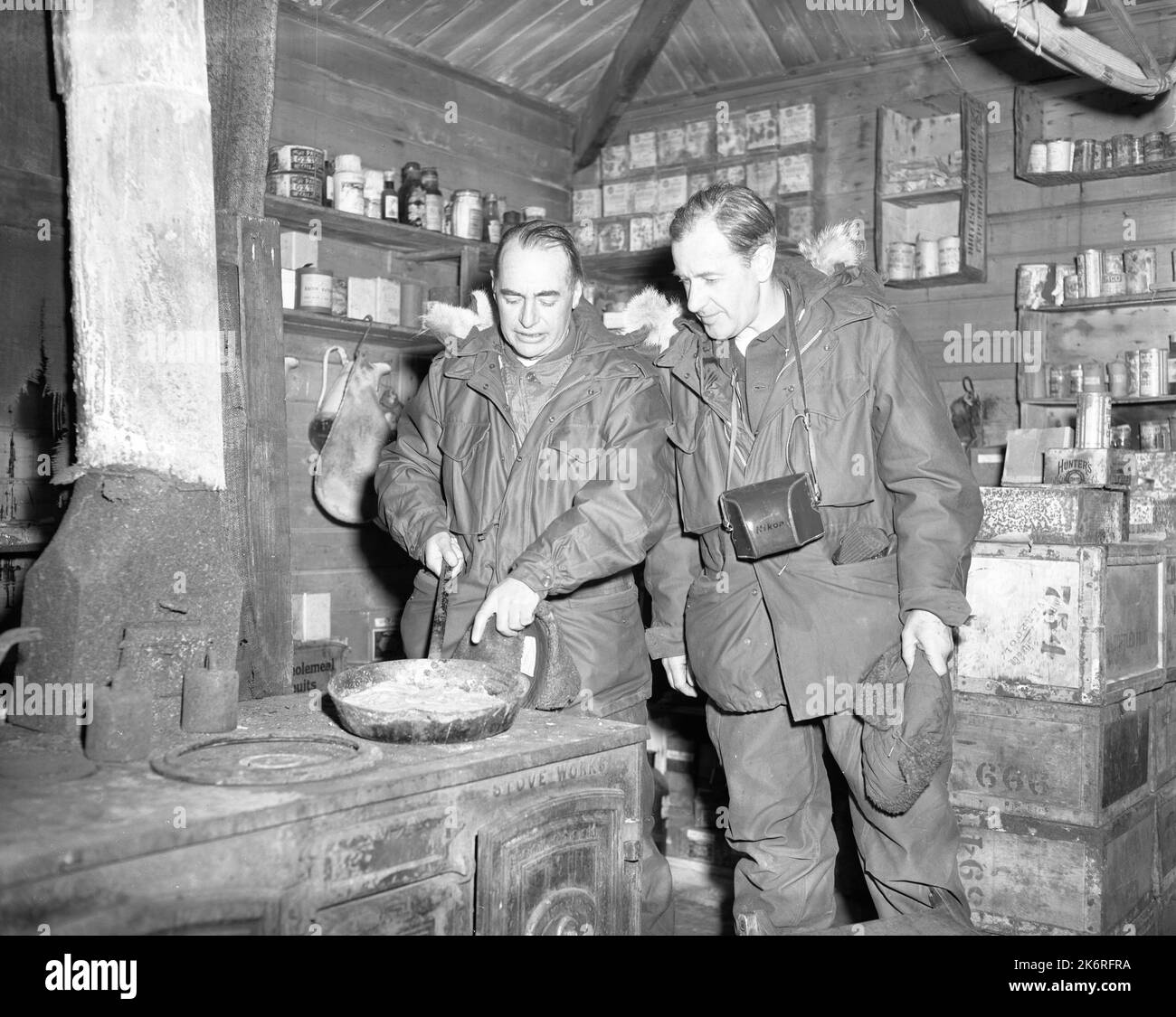 Photographie du Groupe de travail quarante-trois. (De gauche à droite) M. Alan Moorehead, de Porto Ercole (Grosseto), Italie, et M. Sidney Nolan, de Londres, Angleterre, discutant de la poêle à frire laissée dans la hutte de Shackleton à Cape Royds, Antarctique. La cabane a été construite pendant l'expédition britannique en Antarctique (1907-1909). Les gentleman sont sur le continent gelé comme invités de RADM. James R. Reedy, USN, commandant des États-Unis Force navale, Antarctique. Banque D'Images