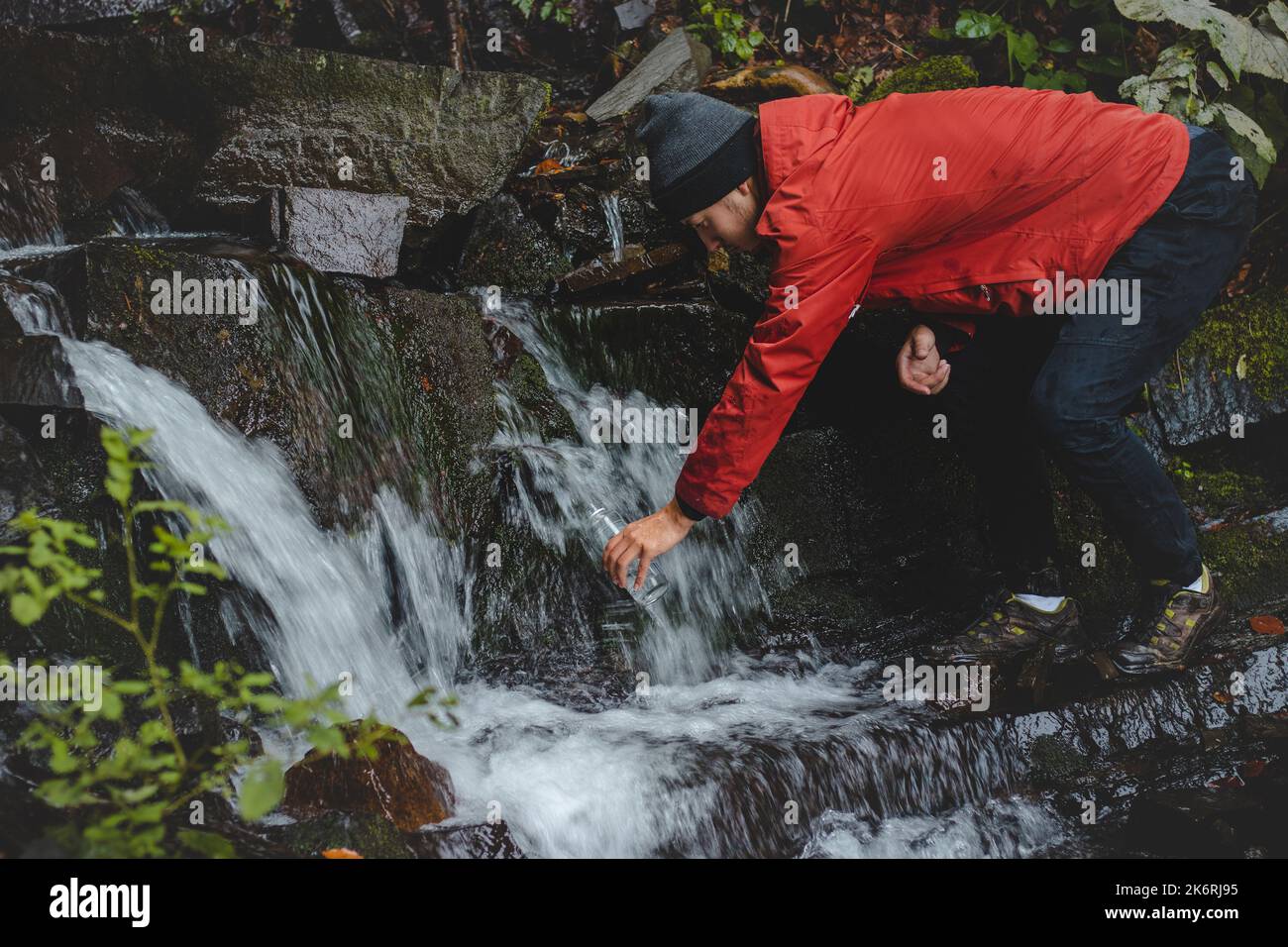 Randonneur sur une longue piste remplit l'eau potable d'une source de montagne dans un récipient en verre. Remplir d'eau propre pour cuisiner et boire tout en étant bien haut Banque D'Images