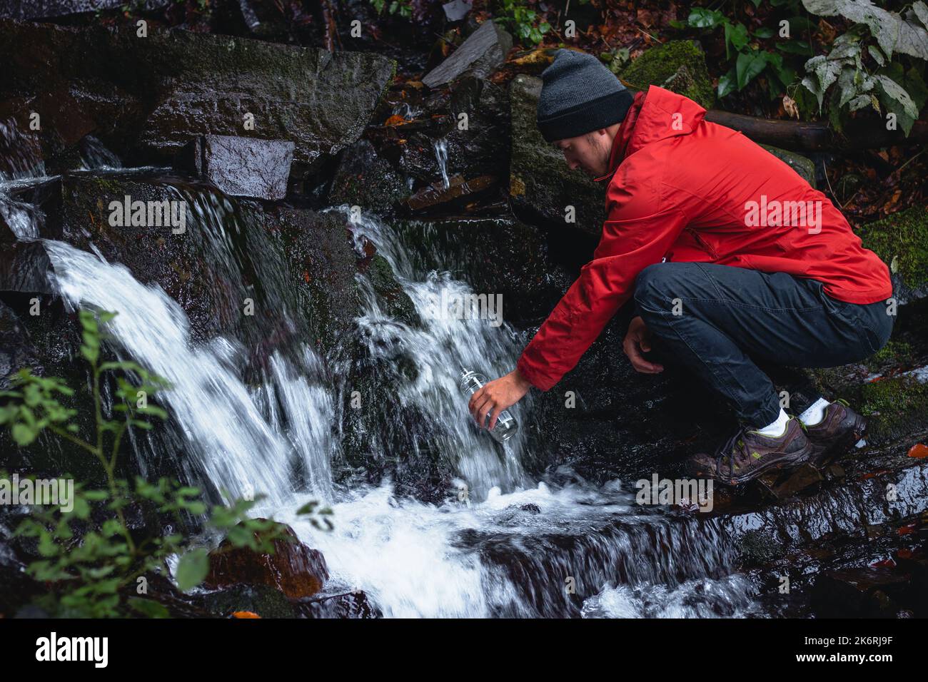 Randonneur sur une longue piste remplit l'eau potable d'une source de montagne dans un récipient en verre. Remplir d'eau propre pour cuisiner et boire tout en étant bien haut Banque D'Images