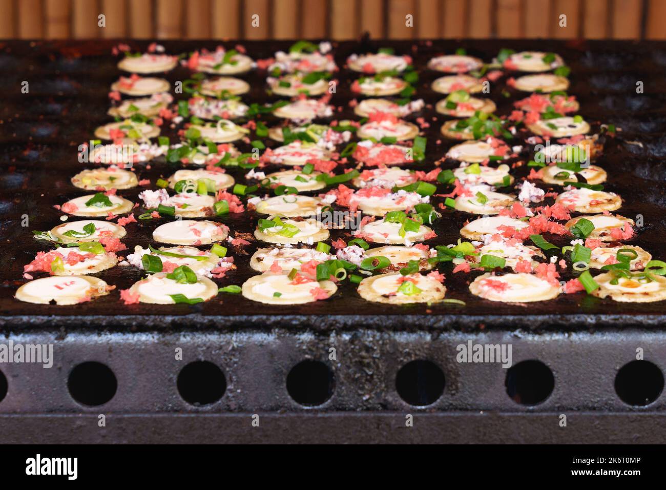 Cuisine de rue japonaise takoyaki dans une poêle spéciale. Processus de cuisson des boulettes de takoyaki avec remplissage de poulpe. En-cas japonais et repas de rue au fes Banque D'Images