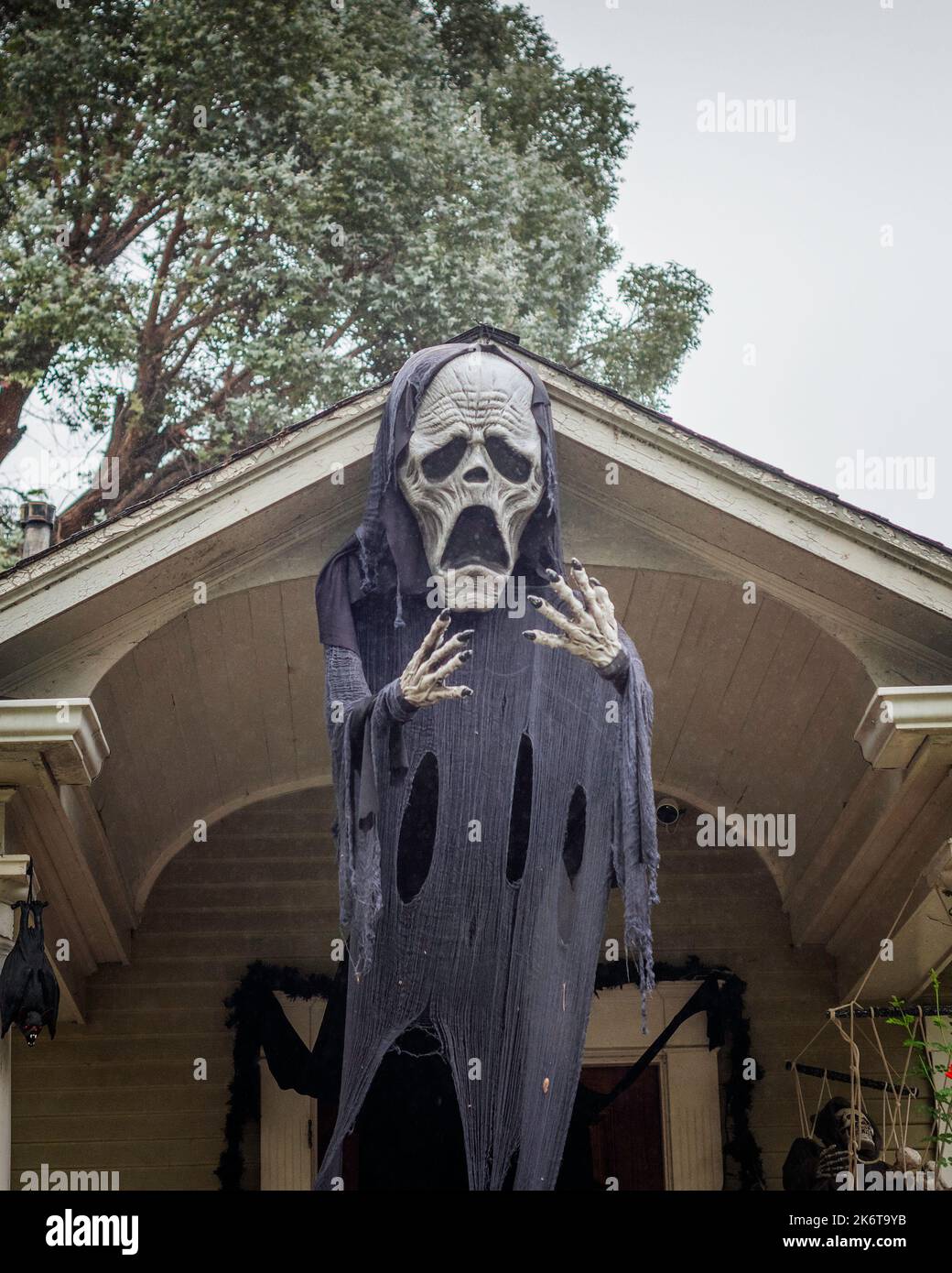 Une grande figure de la mort dans un manteau noir est suspendue devant l'entrée d'une maison. Banque D'Images