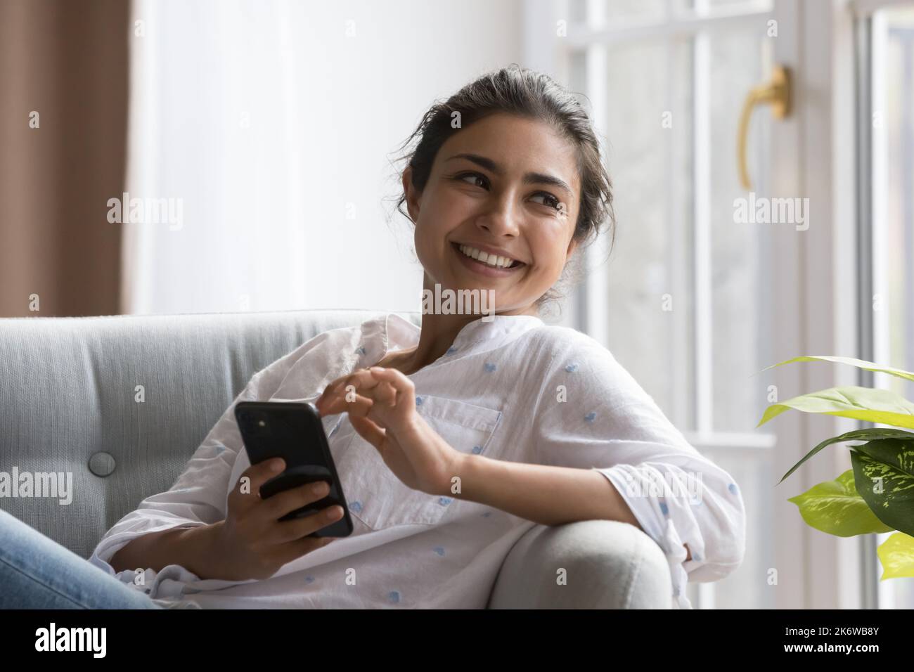 Femme indienne paisible se détendant sur une chaise confortable avec un smartphone Banque D'Images