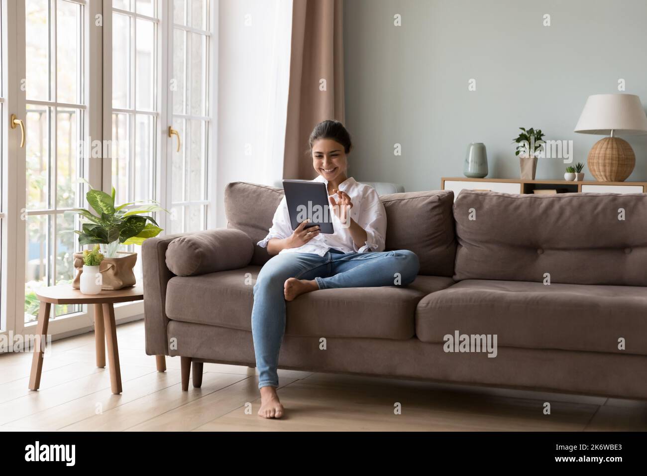 Jolie femme indienne utilisant une tablette numérique assise sur un canapé Banque D'Images