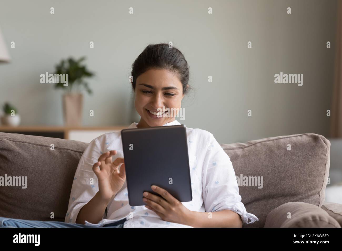 Une femme indienne est assise sur un canapé avec une tablette numérique moderne Banque D'Images