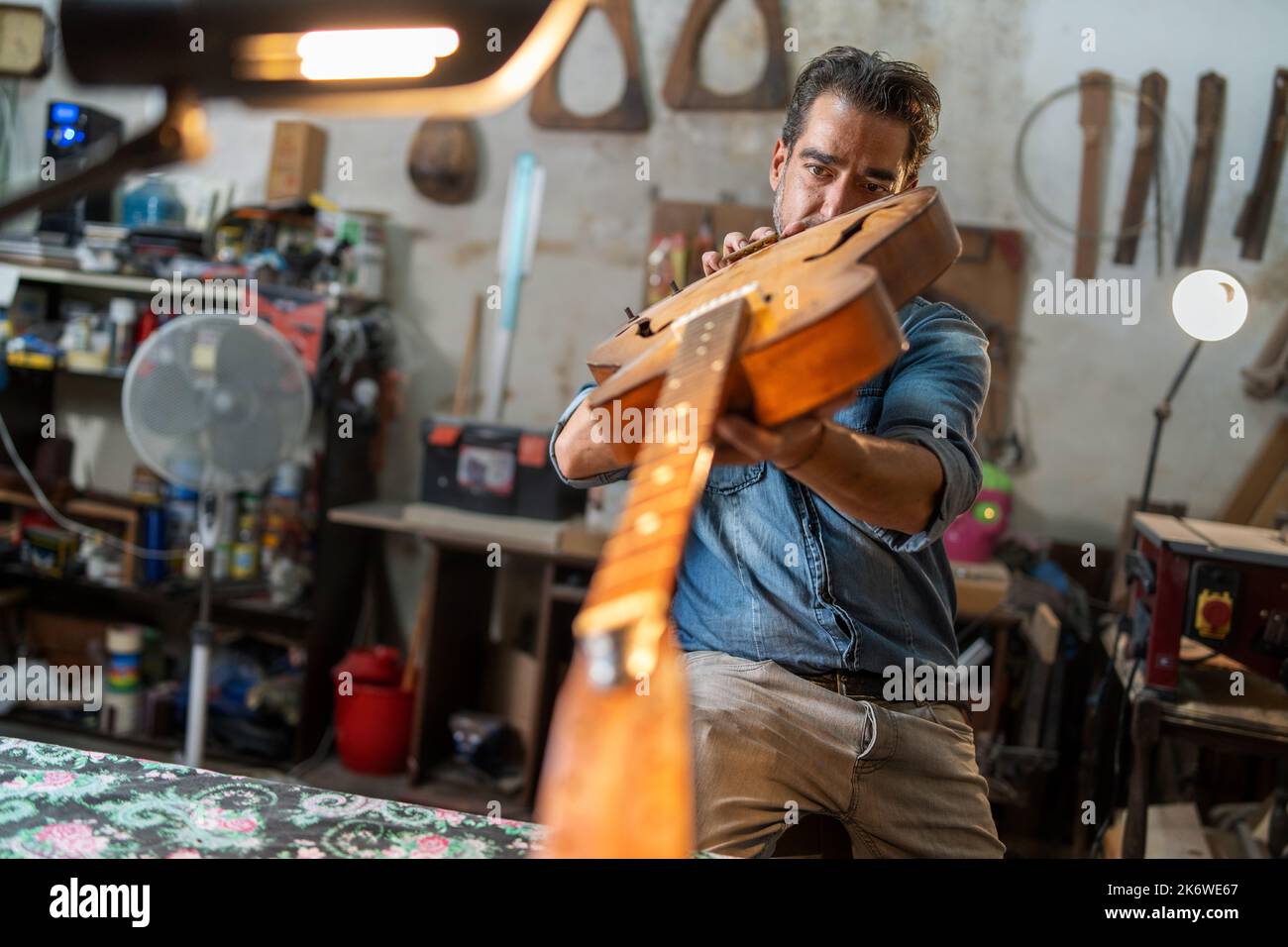 Un luthier répare une guitare semi-acoustique d'époque en regardant le cou et les fingerboard à l'intérieur d'une ancienne lutherie artisanale - petit bussin artisanal Banque D'Images