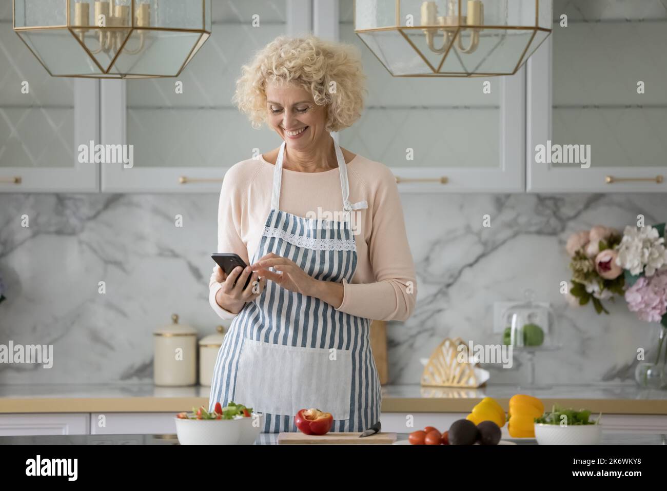 Une femme plus âgée utilise un smartphone seul dans une cuisine moderne Banque D'Images