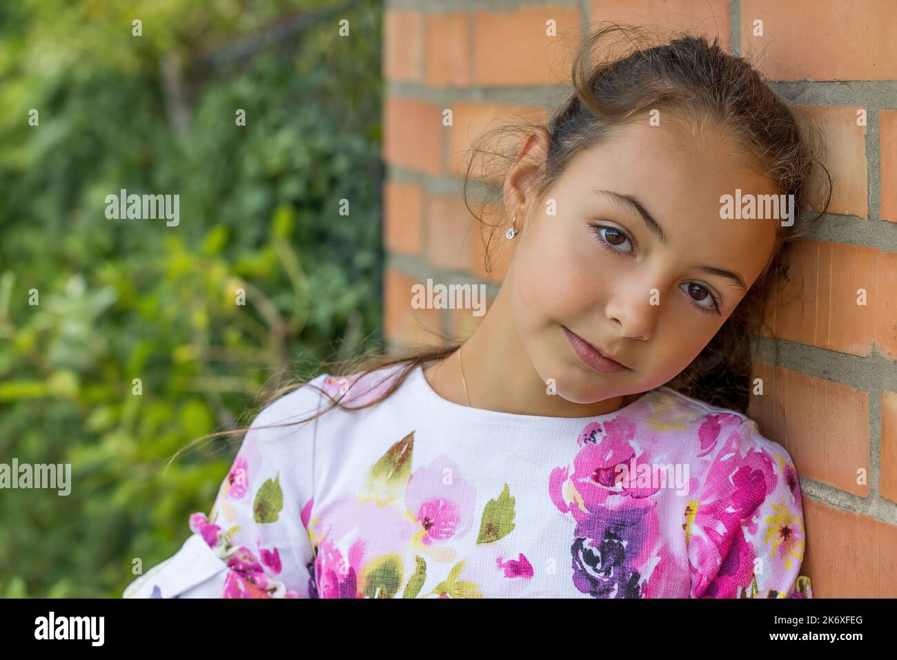 Petite fille mignonne pose avec sa tête reposant sur un mur de brique. Horizontalement. Banque D'Images