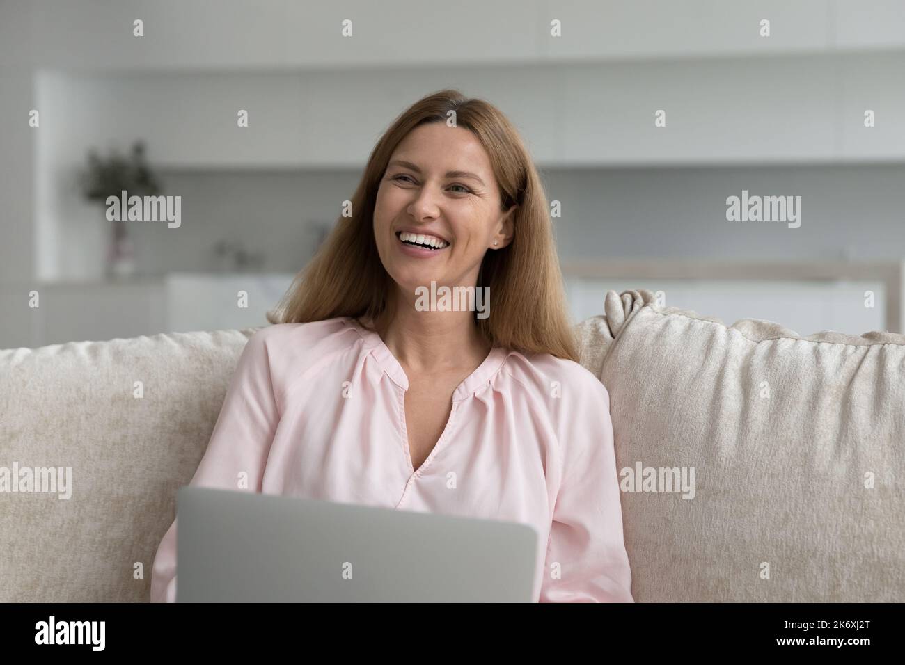 Belle femme riante s'asseoir sur un canapé avec un ordinateur portable Banque D'Images