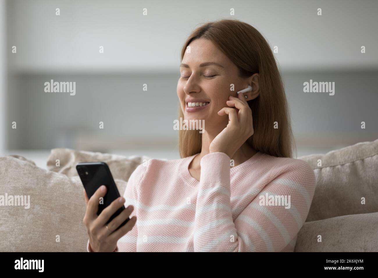 Sereine femme porte des écouteurs utiliser le téléphone portable écouter de la musique à la maison Banque D'Images