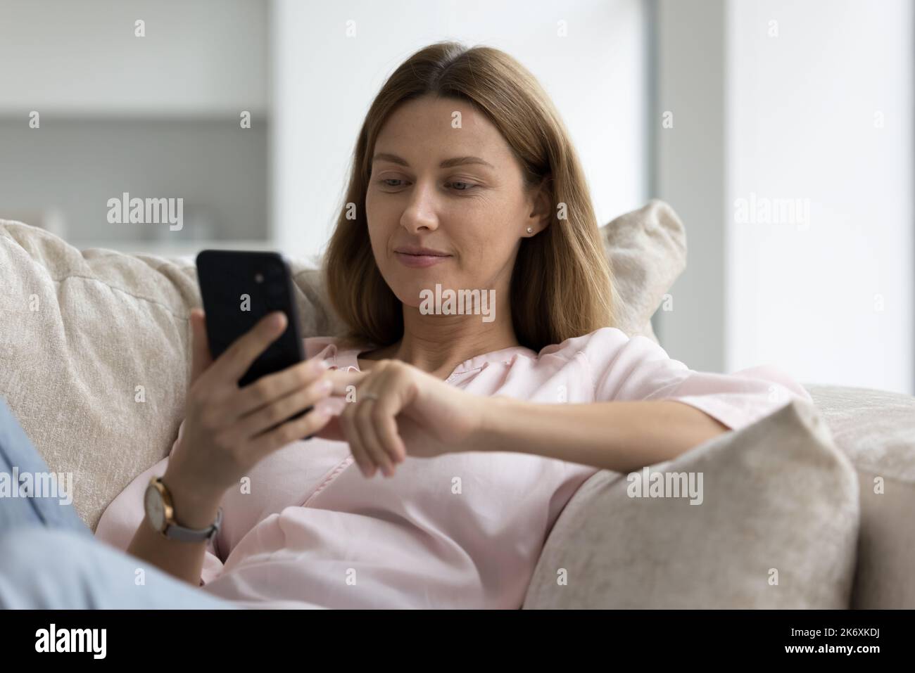 Une jeune femme se repose sur un canapé à l'aide d'un smartphone moderne Banque D'Images